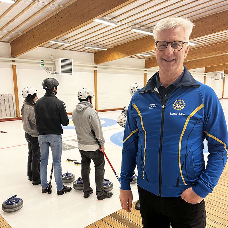 Ledaren Lars-Åke Linander i curlingklubben Granits lokaler, några personer spelar curling i bakgrunden.