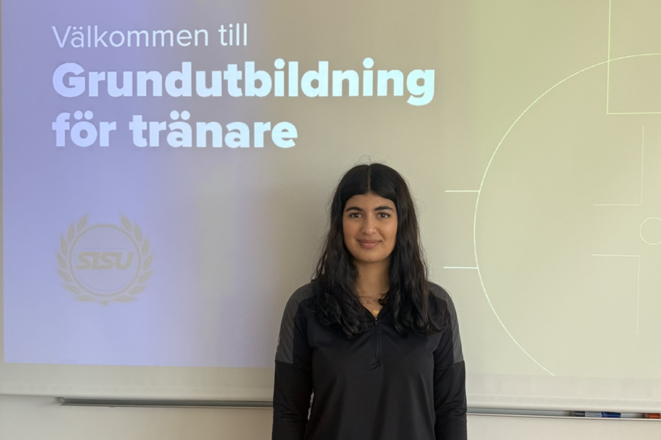 Andia Jamfar framför en bakgrund med texten "Välkommen till Grundutbildning för tränare" och logotypen "SISU". Personen bär en svart sporttröja.